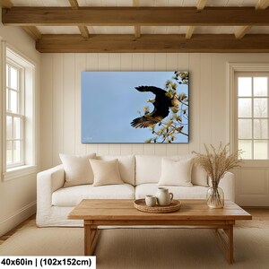 May include: A framed canvas print showing a bald eagle in flight against a blue sky. The eagle, with its dark brown body and white head, is perched on a tree branch. The artwork measures 102x152cm.