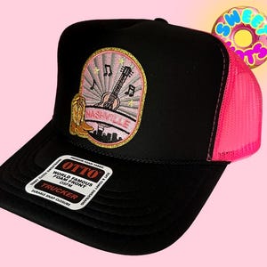 Può includere: Cappellino da camionista nero con retro in rete rosa e toppa Nashville. La toppa presenta una chitarra, uno stivale da cowboy e il nome della città. Il cappellino ha una visiera curva e una chiusura a scatto.