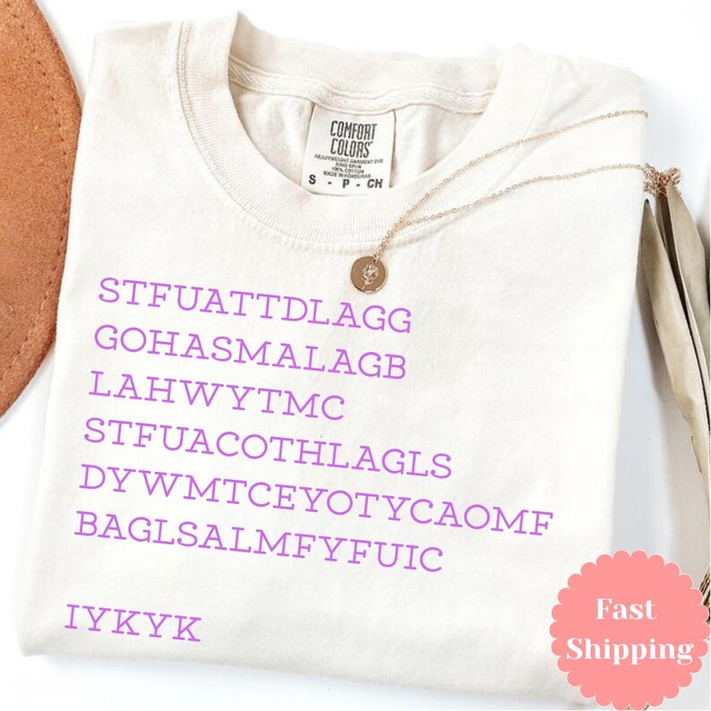 Puede incluir: Camiseta Comfort Colors color crema con texto morado y collar dorado. El texto incluye el acr&oacute;nimo "IYKYK" y otras palabras. Tambi&eacute;n es visible una pegatina rosa con las palabras "Fast Shipping".