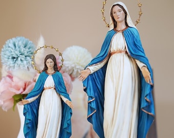 Op de afbeelding: Twee beelden van de Maagd Maria in verschillende formaten, elk gekleed in een wit gewaad en een blauwe mantel met gouden rand. Beide figuren hebben een goudkleurige halo versierd met kleine sterren en staan op een donkerblauwe wereldbol.