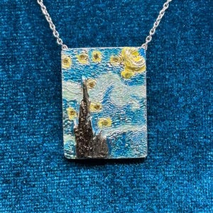 Può includere: Collana color argento con un ciondolo rettangolare raffigurante "La notte stellata" di Van Gogh. Il ciondolo mostra una pittura in miniatura strutturata e colorata del cielo notturno, con un albero scuro e stelle gialle.