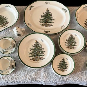 May include: A complete Christmas-themed dinnerware set featuring white plates, bowls, and serving dishes with a green tree design and green trim. Includes teacups and saucers, and a small teapot.