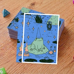 May include: A stack of blue playing cards featuring a whimsical illustration of a frog wearing a wizard hat, sitting on a lily pad. The background is a blue pond with stars and other magical elements.