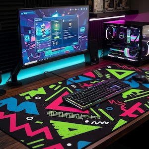 May include: A gaming setup featuring a black keyboard with RGB lighting, a mouse, and a large monitor displaying a game interface. The desk has a colorful mousepad with geometric shapes in pink, green, and blue. A computer tower with RGB lights is also visible.