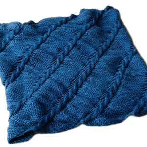 Könnte beinhalten: Eine gestrickte blaue Decke mit einem strukturierten Muster. Die Decke hat diagonale Reihen erhabener Maschen und einen gewellten Rand. Die Farbe ist ein tiefes, sattes Blau, und die Textur wirkt weich und einladend.