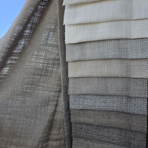May include: A collection of fabric swatches in various shades of gray and white, arranged in a layered display. The fabrics have a textured appearance, with visible weave patterns. A larger piece of matching fabric is draped on the left.