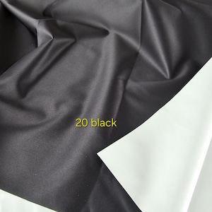 Puede incluir: Una pieza de tela con textura suave y mate, que presenta un lado negro profundo y un lado blanco contrastante. El material est&aacute; drapeado en pliegues suaves, y el texto 20 black est&aacute; impreso en amarillo sobre la superficie oscura de la tela.