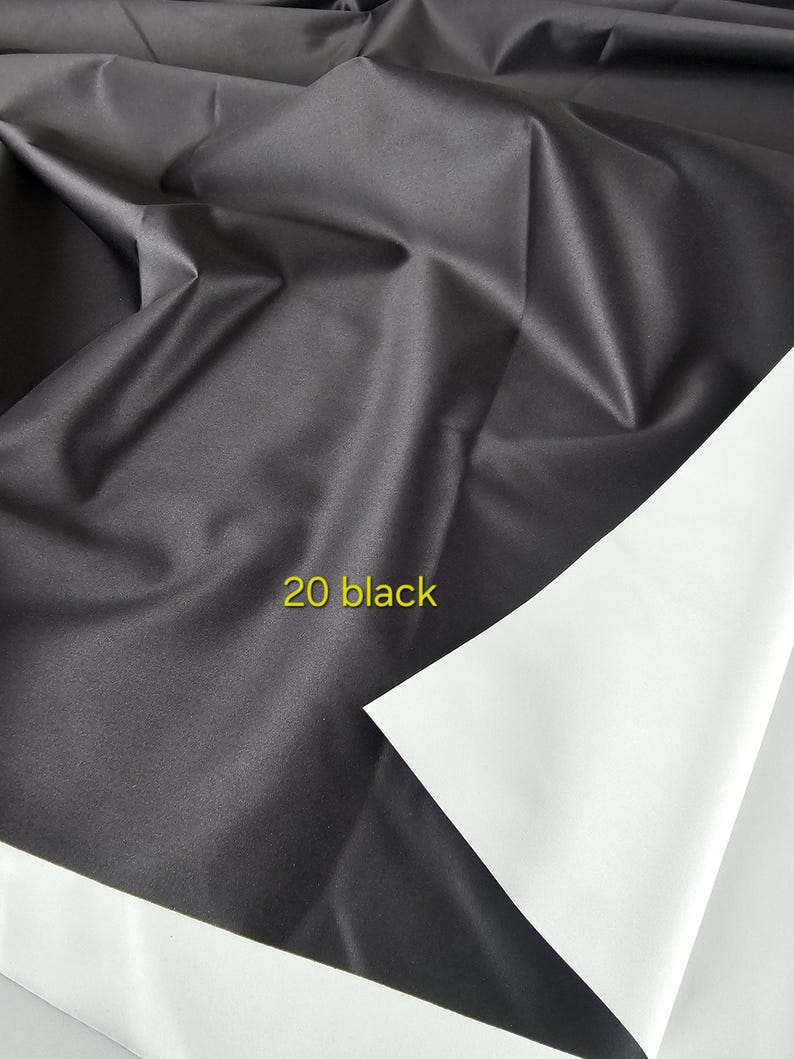 Puede incluir: Una pieza de tela con textura suave y mate, que presenta un lado negro profundo y un lado blanco contrastante. El material est&aacute; drapeado en pliegues suaves, y el texto 20 black est&aacute; impreso en amarillo sobre la superficie oscura de la tela.