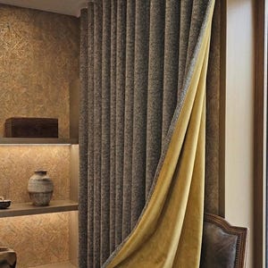 Puede incluir: Cortinas de ventana en capas en un entorno de habitación. La capa exterior es de tela marrón oscuro texturizada, mientras que la capa interior es de terciopelo amarillo mostaza. Una silla de cuero marrón está en primer plano. Ambiente cálido.