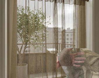 Puede incluir: Cortina de ventana transparente y tejida en color beige neutro. La cortina está colgada de una barra de madera y permite que la luz se filtre. La cortina está atada en la parte inferior. Se ve un árbol a través de la ventana.