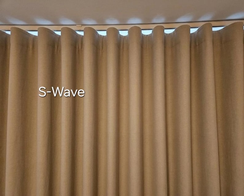 Puede incluir: Una cortina de color tostado con un patr&oacute;n de pliegues en forma de S-Wave que cuelga de un sistema de rieles. La tela muestra una textura uniforme y suave con pliegues verticales que crean un efecto de onda repetitivo en todo el ancho.