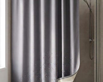 Puede incluir: Una cortina de ducha gris sólida colgada de una barra de metal con anillos plateados. La cortina presenta un patrón impreso de gotas de agua transparentes concentradas en el borde inferior. La esquina inferior está doblada para mostrar un forro.