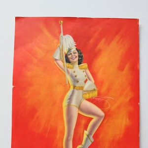 May include: A woman in a white and gold uniform with a white feathered hat holds a baton and poses against a red and orange background.