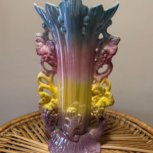 Könnte beinhalten: Eine farbenfrohe Keramikvase mit einem Farbverlauf von Blau, Rosa und Gelb. Die Vase hat ein einzigartiges Design mit filigranen Blumendetails und einem gewellten Rand.