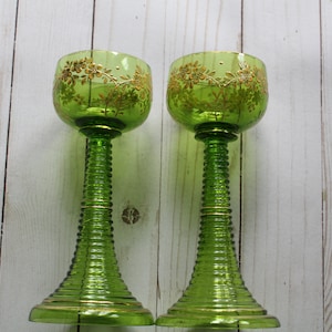 May include: Two green glass goblets with gold trim and floral designs. The goblets have a ribbed stem and a wide bowl.