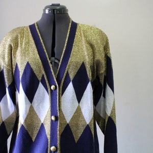 May include: A vintage argyle cardigan in gold, navy blue, and white. The sweater features a V-neck, long sleeves, and gold buttons. The argyle pattern is a classic diamond design. The cardigan is displayed on a black dress form.