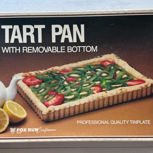 Puede incluir: Molde rectangular para tarta con fondo extraíble, relleno de rodajas de kiwi y fresas. La caja dice "TART PAN WITH REMOVABLE BOTTOM" y "PROFESSIONAL QUALITY TINPLATE". La tartera está sobre un fondo marrón con una tetera blanca y limones en rodajas.