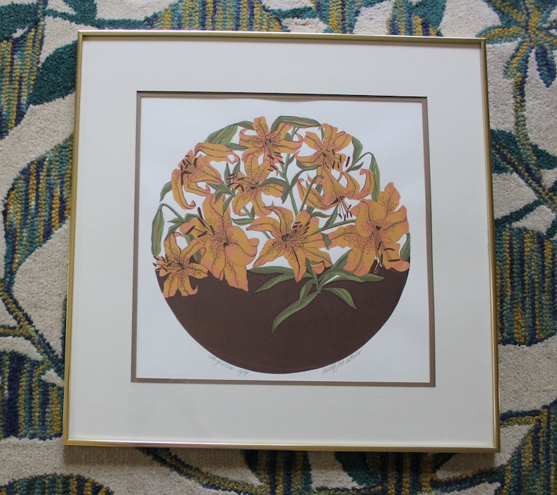May include: A framed print of a stylised illustration of orange lilies in a brown vase. The print is titled "Lily in Bloom" and signed by the artist.