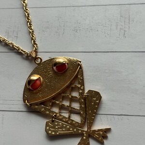 Pode incluir: Colar com pingente de rã em metal dourado. O pingente de rã tem detalhes em vermelho e dourado para os olhos. O corpo da rã tem um design de treliça. A corrente do colar também é dourada.