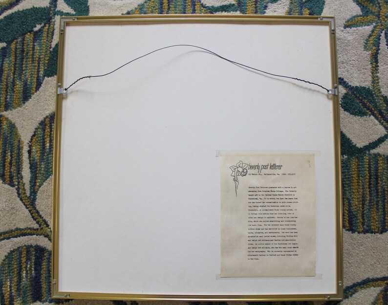 May include: A framed print with a gold frame and a white mount. The print features a black and white illustration of a flower with a text description of "Beverly Paul Letterer" and a short biography of the artist.