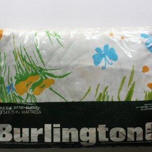 Könnte beinhalten: Ein weißes Spannbettlaken mit einem Blumendruck in Grün-, Gelb- und Blautönen. Die Verpackung enthält den Text "One Buy Fitted Sheet for 54x75 in. Mattress" und "Burlington".
