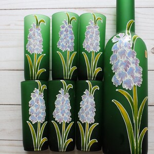 Puede incluir: Un juego de seis vasos verdes y una botella a juego. Cada vaso y la botella est&aacute;n decorados con un dise&ntilde;o floral pintado a mano con flores moradas claras, hojas verdes y detalles amarillos.