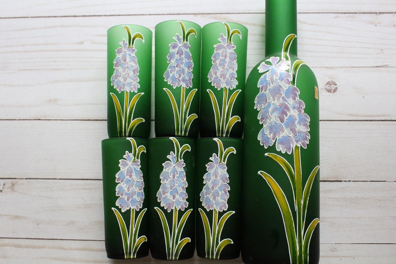 Puede incluir: Un juego de seis vasos verdes y una botella a juego. Cada vaso y la botella est&aacute;n decorados con un dise&ntilde;o floral pintado a mano con flores moradas claras, hojas verdes y detalles amarillos.