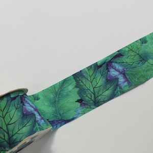 May include: A roll of green and blue patterned ribbon with a watercolor leaf design. The ribbon is rolled up on a cardboard spool.