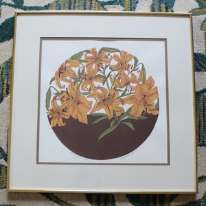 May include: A framed print of a circular design featuring a cluster of orange lilies with brown and green accents. The print is titled "Lily and Lilies" and signed by the artist.