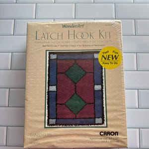 May include: A WanderArt Latch Hook Kit in a tan box with a stained glass pattern rug illustration. The box features the text Latch Hook Kit, Stained Glass, and Caron, with a yellow sticker stating Fast Fun New Easy To Do. Dimensions are 20 inches by 27 inches.