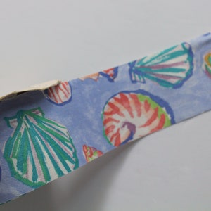 May include: A blue ribbon with a repeating pattern of colorful seashells. The ribbon is made of fabric and has a slightly textured surface.