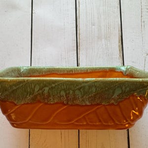 May include: A rectangular ceramic planter with a green and orange glaze. The planter has a wavy, textured design.