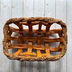 Puede incluir: Una cesta tejida de forma rectangular. Está hecha de un material marrón claro, con un diseño de celosía. Los bordes están decorados con semillas. La cesta está vacía y descansa sobre una superficie de madera clara. Medidas: 30 cm x 20 cm.