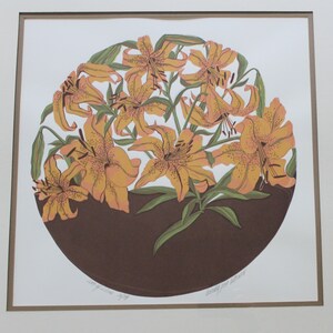 May include: A framed print of a circular design featuring a cluster of orange lilies with brown stems and leaves on a brown background. The print is signed "Dorothy West Halloran".