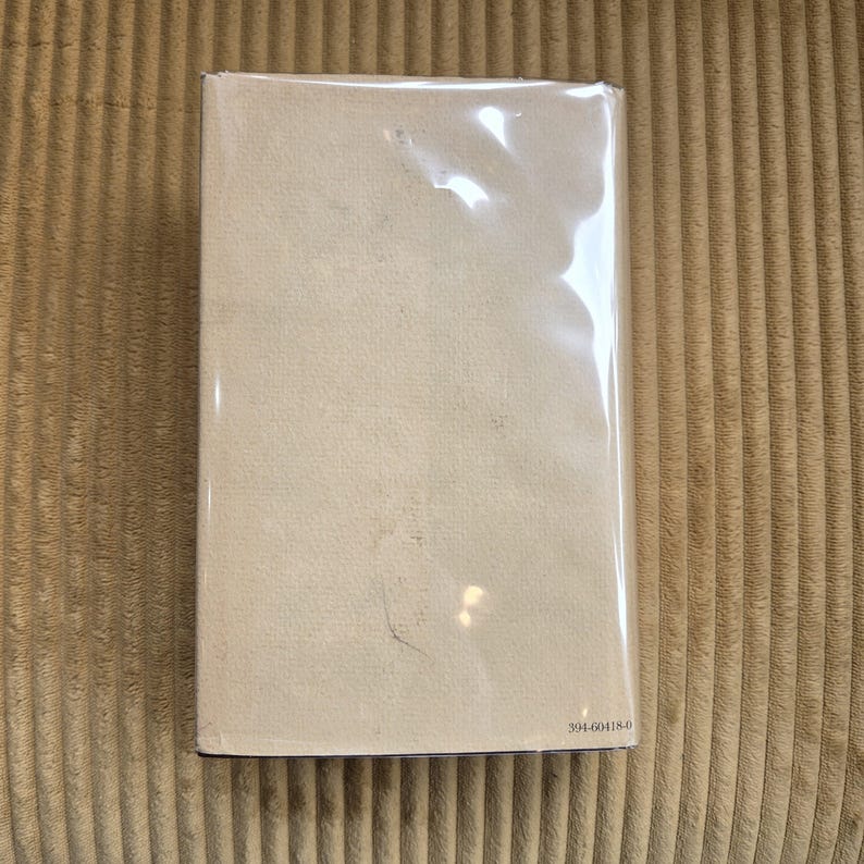 May include: A rectangular book encased in transparent plastic. The book features a pale beige cover with a lightly textured finish. The number "394-60418-0" is visible in the bottom right corner.