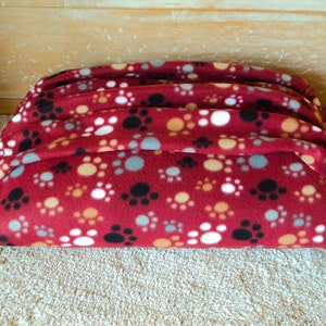 May include: Red fleece dog bed with a paw print pattern in white, brown, and grey.