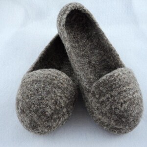 Puede incluir: Un par de zapatillas sin cordones confeccionadas en lana afieltrada de color marr&oacute;n y gris jaspeado. Las zapatillas presentan un dise&ntilde;o de punta redondeada, una abertura baja y una superficie densa y texturizada propia del material natural.