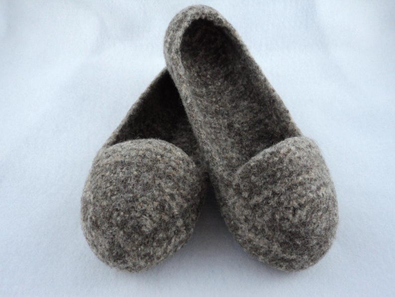 Puede incluir: Un par de zapatillas sin cordones confeccionadas en lana afieltrada de color marr&oacute;n y gris jaspeado. Las zapatillas presentan un dise&ntilde;o de punta redondeada, una abertura baja y una superficie densa y texturizada propia del material natural.