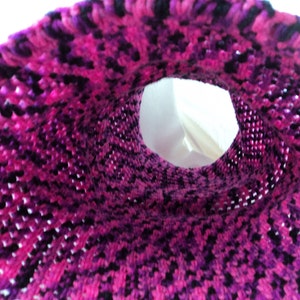 May include: A close-up of a pink and purple crocheted fabric with a hole in the centre. The fabric is made of yarn and has a textured surface.
