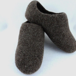 May include: A pair of dark brown felted wool slippers with a rounded toe and a slip-on design. The slippers feature a dense, textured surface and a solid dark brown color throughout, showcasing a simple construction with no visible seams or closures.