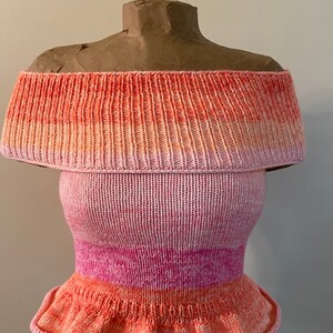 May include: Off-the-shoulder knitted top with a pink and orange ombre design. The top has a ruffled hem.
