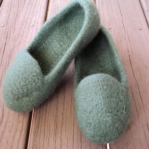 Puede incluir: Un par de zapatillas de lana afieltrada en color verde salvia con punta redondeada y dise&ntilde;o sin cordones. Las zapatillas presentan un material grueso y texturizado con una superficie suave y difusa y una abertura profunda para el pie.