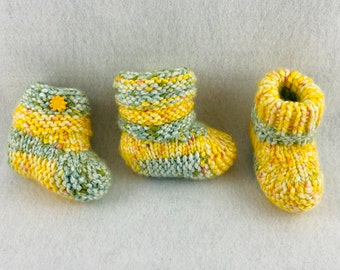 May include: Three pairs of knitted baby booties in yellow and green stripes. One pair has a yellow button in the shape of a flower.