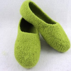 May include: A pair of lime green felted wool slippers with a rounded toe and a slip-on design. The slippers feature a textured, fuzzy surface and a deep opening, showcasing the dense, matted wool construction of the footwear.