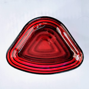 May include: A red glass bowl with black concentric circles around the rim. The bowl is triangular in shape.