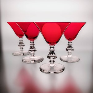 May include: Four red glass martini glasses with clear stems and bases. The glasses are arranged in a row, with the front glass slightly offset from the others.