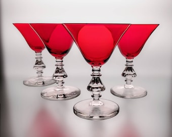 May include: Four red glass martini glasses with clear stems and bases. The glasses are arranged in a row, with the front glass slightly offset from the others.