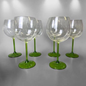 May include: A set of six clear wine glasses. Each glass has a green stem and base. The glasses are arranged together. The green stems and bases provide a contrast to the clear glass.