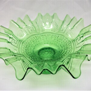 May include: A green glass bowl with a ruffled edge and a geometric pattern on the bottom. The bowl is made of clear glass with a green tint.