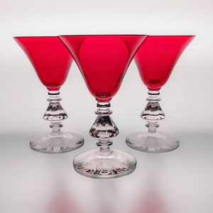 May include: Three red wine glasses with clear stems and bases. The glasses have a wide bowl and a narrow stem.